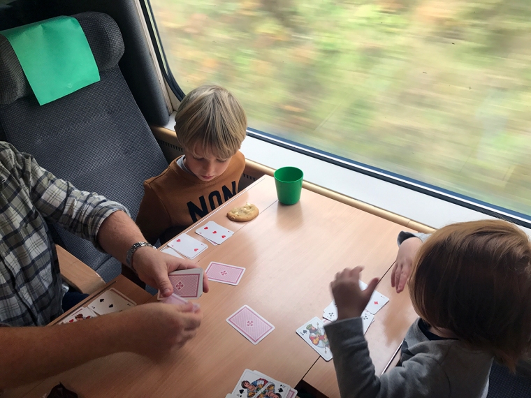 Tåv barn och en vuxen spelar kort på ett tåg.