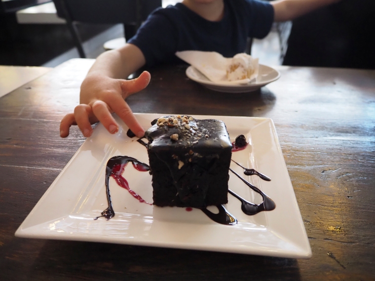 Vit kvadratisk tallrik med en brun chokladkaka på. Ett barns finger som petar på kakan.
